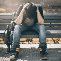 person with head in hands on park bench